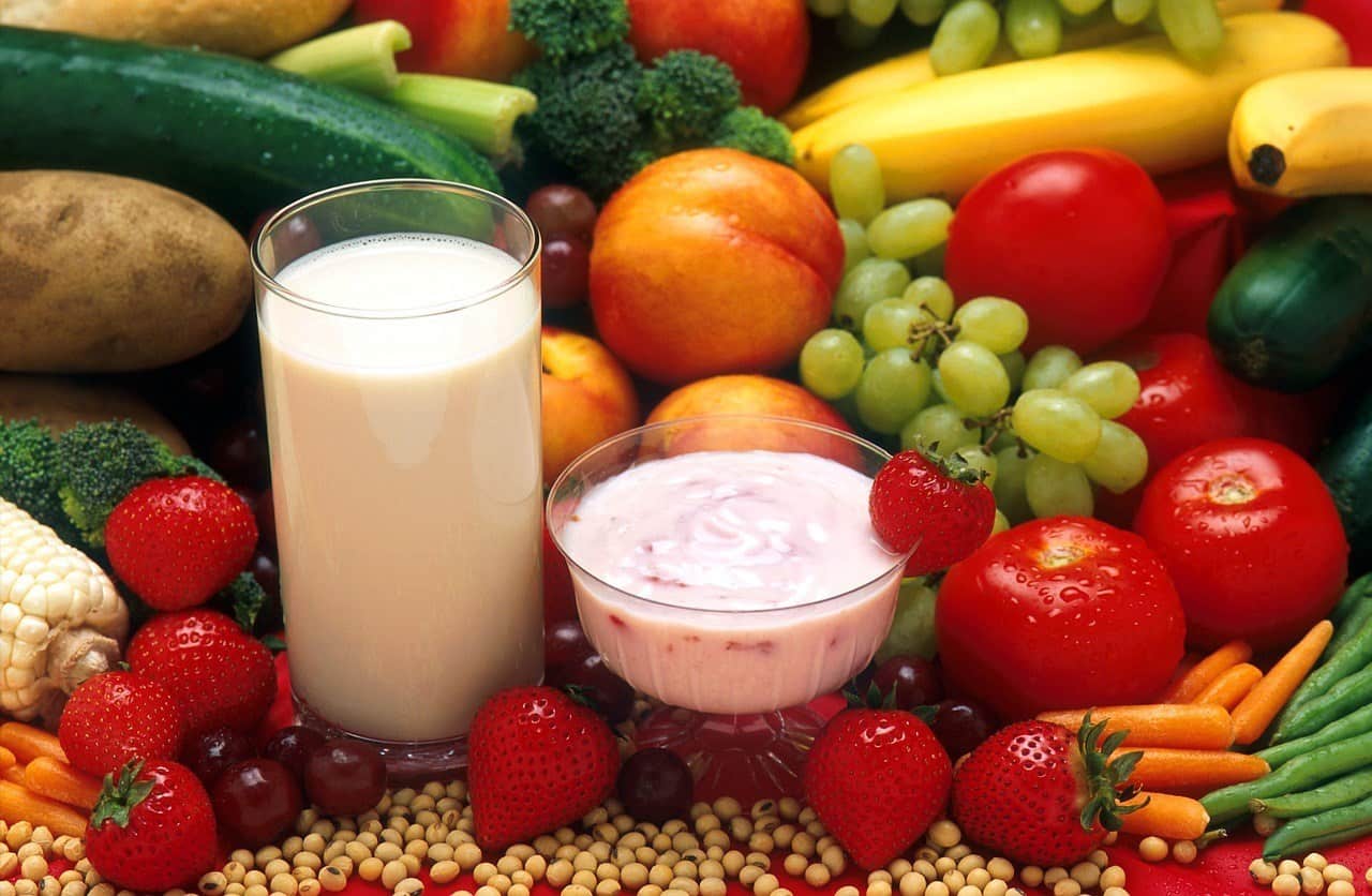 Glasses of milk and a red smoothie surrounded by fruit.