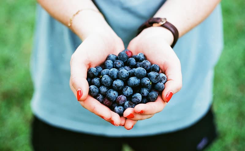 Woman holding blueberries in her palms outdoors.