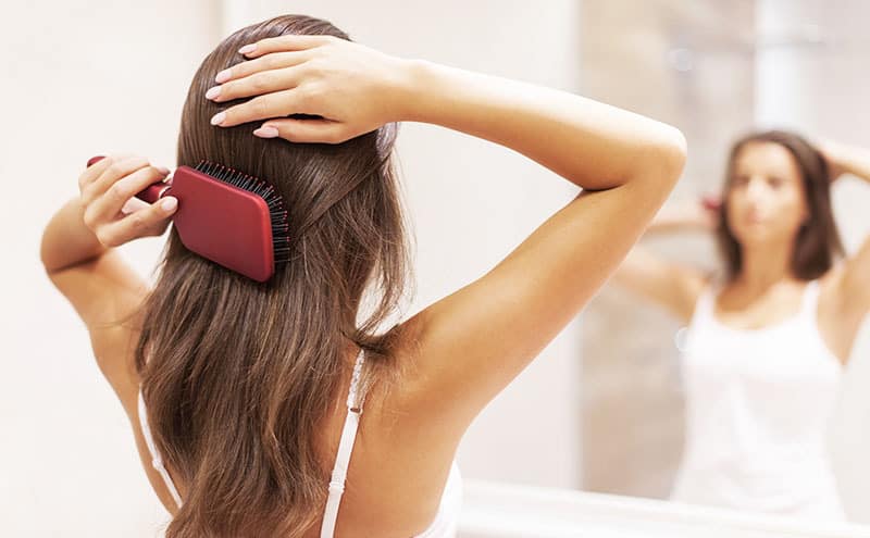 Woman brushing her hair in front of the mirror, wondering what causes dandruff.