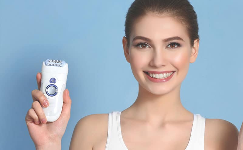 Woman smiling at us as she's showing off her best electric razor for women in front of light blue background.