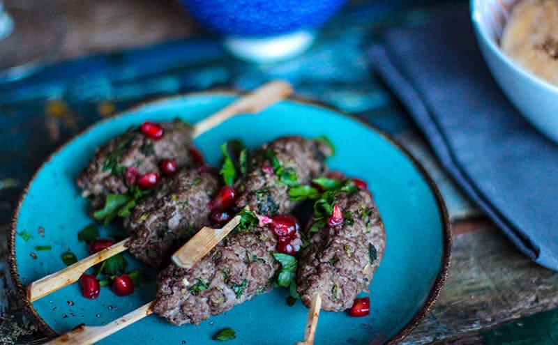 Meatballs on wooden sticks with red berries, on a blue plate, on a wooden table.