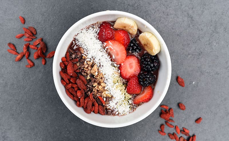 A bowl of goji berries, with walnuts, strawberries, mulberries, banana and coconut on grey background