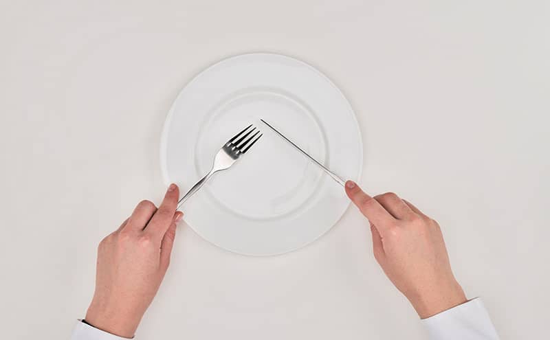 Man using forks and knives on a perfectly empty white plate.