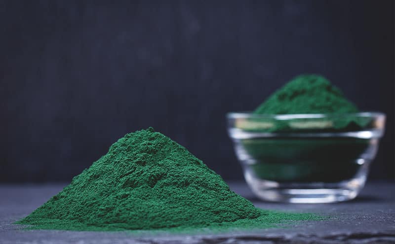 A pile of the best spirulina powder in front of a glass bowl of it.