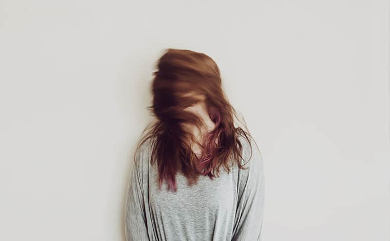 Woman standing in front of light grey background, shaking her hair in a way that it hides her face.