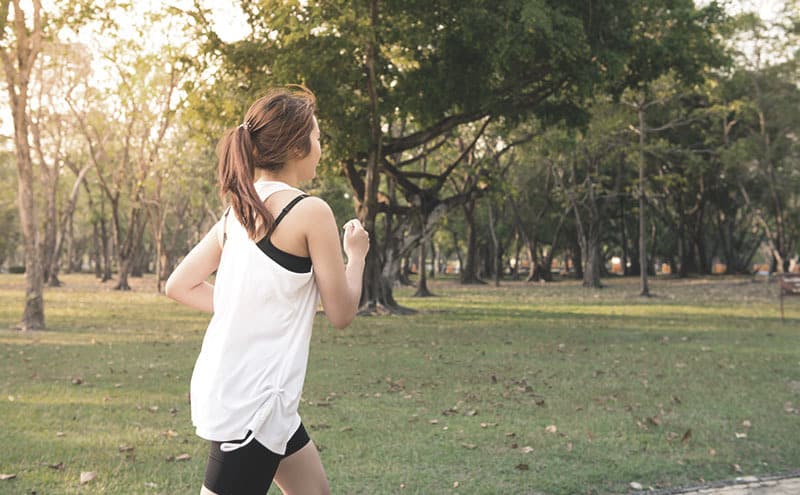 A woman in a white shirt jogging in a park and following her progress with the best fitness tracker for women.