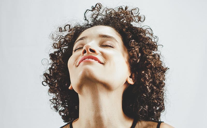 Smiling woman with curly hair enjoying the benefits of the best shampoo for permed and colored hair.