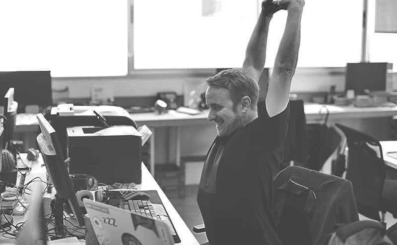 A man gleefully stretching in an office at his desk after he finished a quick exercise with one of the best pedal exercisers.