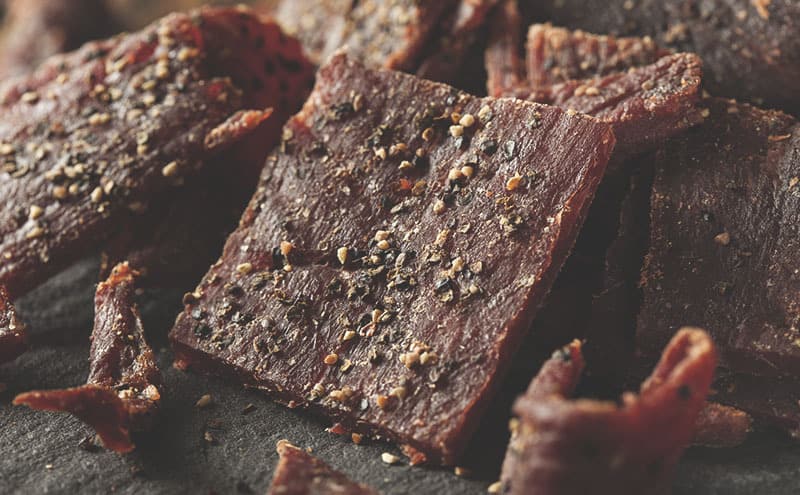 Black peppered beef jerky that is healthy for you on a dark surface.